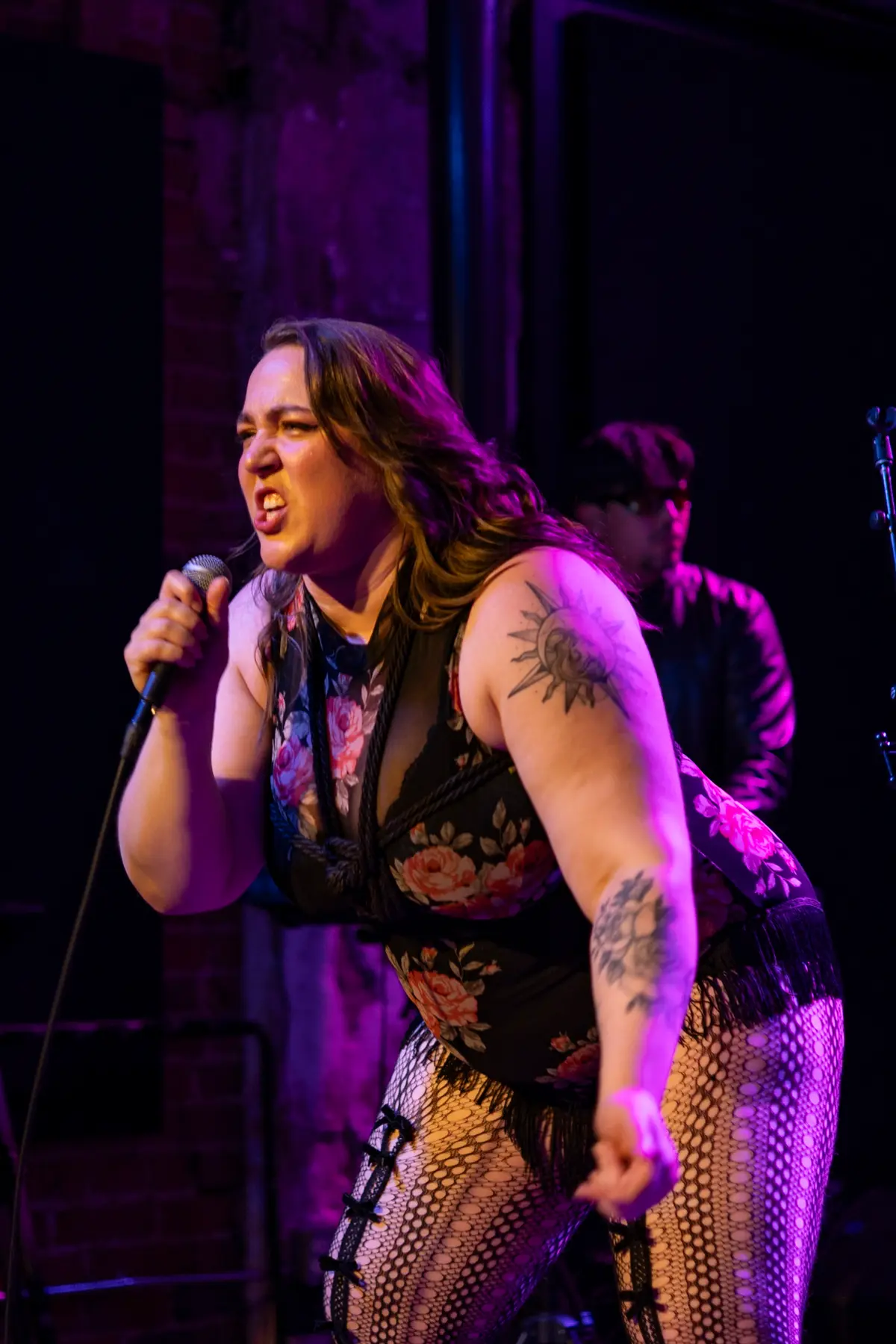 Melissa mid-belt, gripping the mic, leaning into the crowd under pink light.