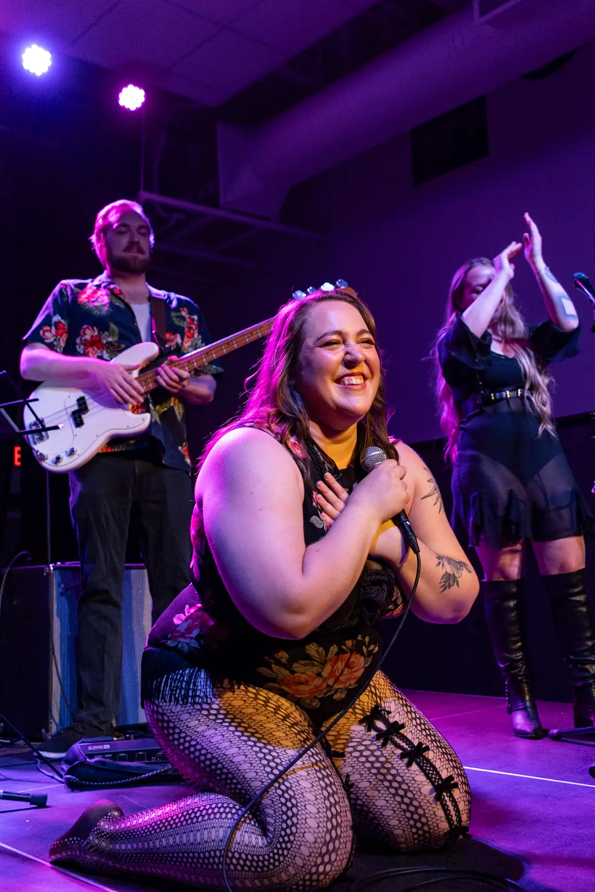 Melissa on her knees at the front of the stage, hand over her heart, band behind her.