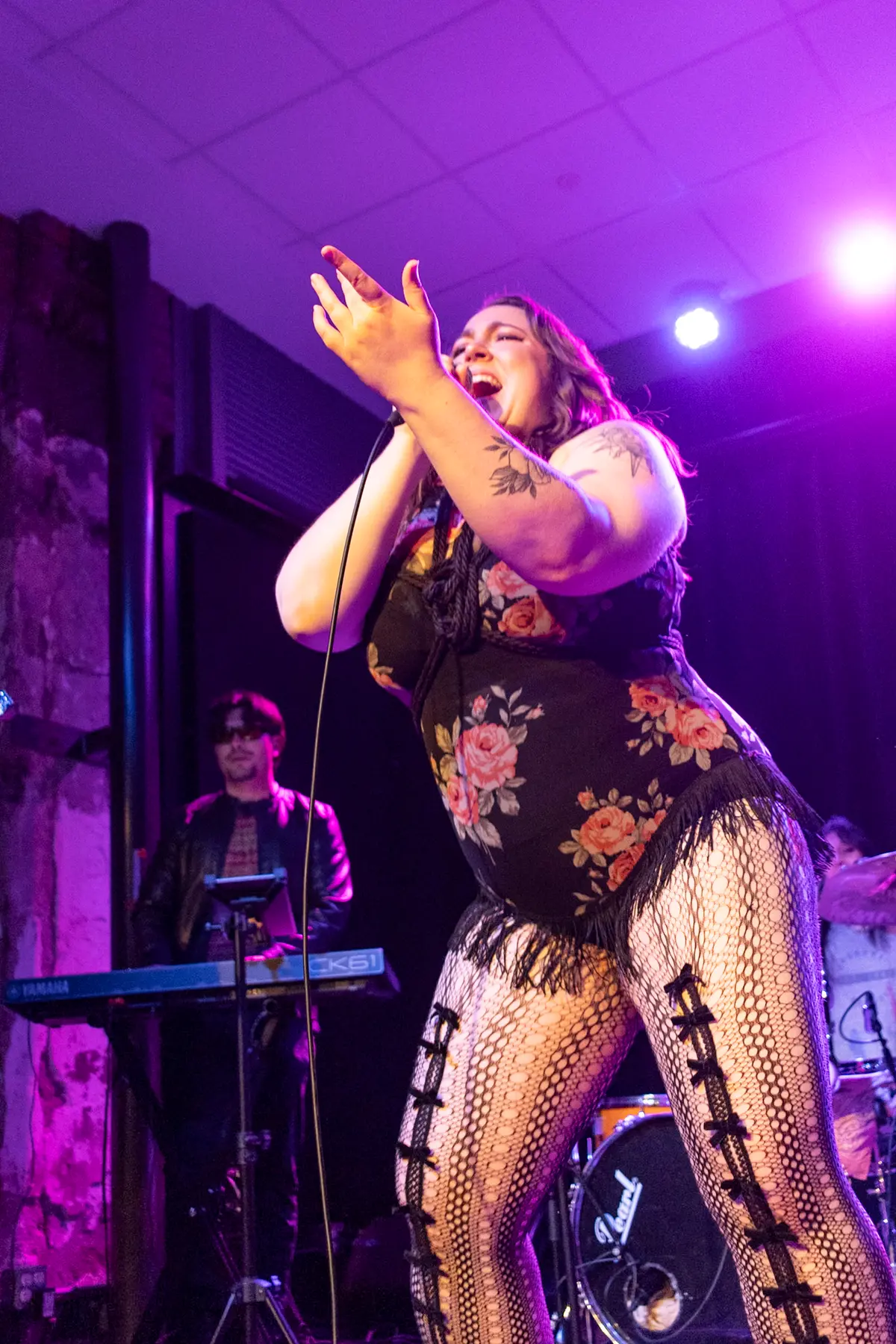 Melissa singing with both hands raised, keys player lit behind her.